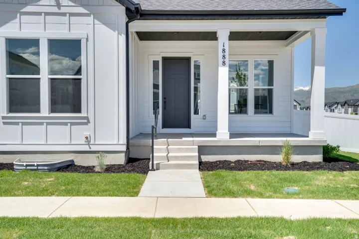 Modern farmhouse exterior featuring white siding, a covered porch with white columns, a dark gray front door, concrete steps, and a manicured lawn