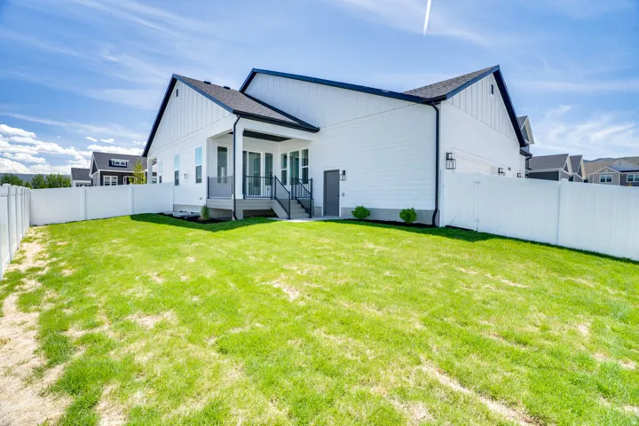 Expansive backyard featuring a manicured lawn, white privacy fencing, and a covered patio with dark railing
