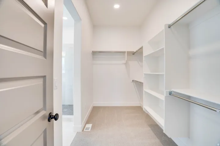 Spacious walk-in closet featuring built-in shelving, multiple hanging rods, recessed lighting, and soft carpeting