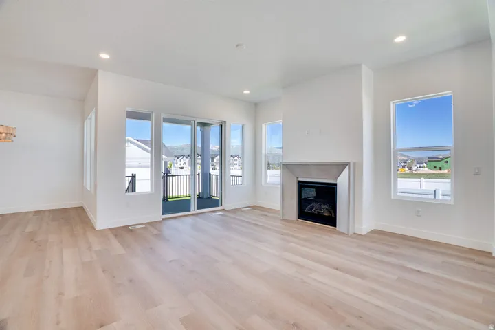 Spacious room featuring wood-finish flooring, a contemporary fireplace with a light-toned mantel, multiple windows, recessed lighting, and a sliding glass door leading to a balcony with black railings