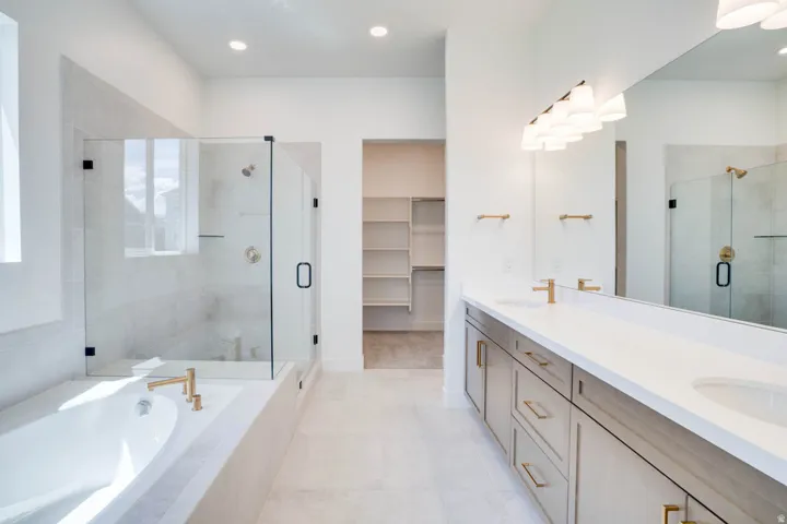 Spacious bathroom featuring a dual vanity with light wood-finish cabinetry, a large frameless mirror, and a built-in soaking tub