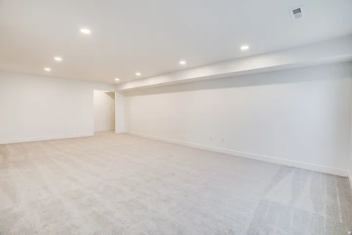 Spacious room featuring plush carpet flooring, recessed lighting, white painted walls, and white baseboards