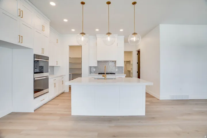Spacious kitchen featuring an expansive center island, white shaker cabinetry with gold-tone hardware, a built-in double oven, and wood-finish flooring