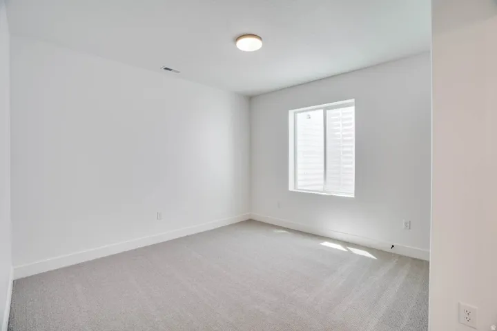 Neutral-toned interior room featuring light gray carpet, white walls, and a single window with blinds