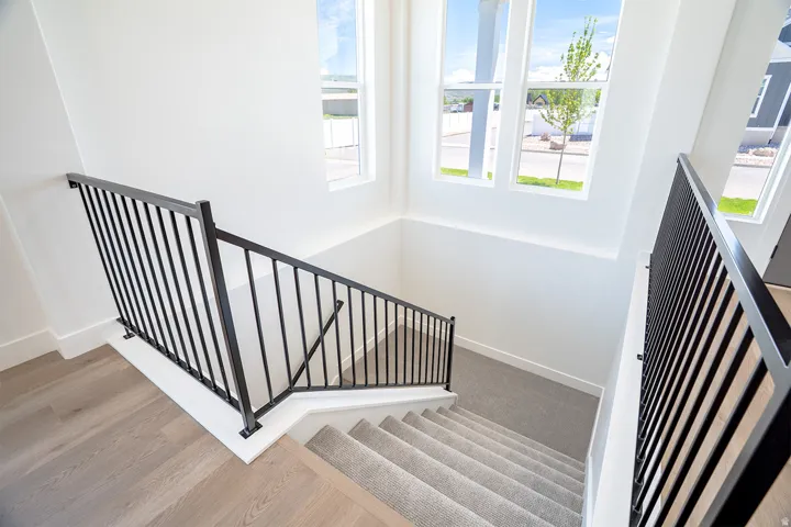 Staircase featuring contemporary black metal railings, light wood-finish flooring, and carpeted treads