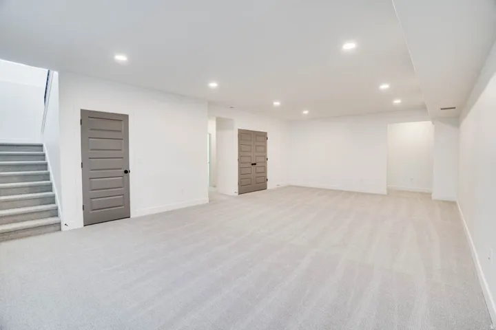Spacious room featuring light-colored carpeting, recessed lighting, white walls, and a staircase with matching carpet