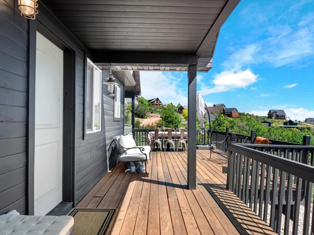 Covered outdoor deck with natural wood-finish flooring, dark wood railings, and a black paneled exterior