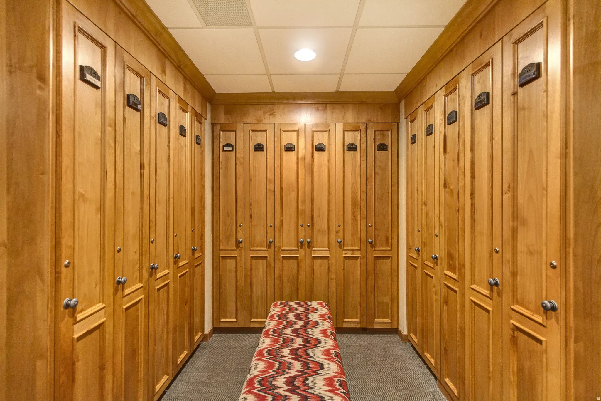 Hallway featuring abundant wood-panel lockers with brushed nickel hardware, recessed ceiling lighting, and a neutral-toned carpeted floor