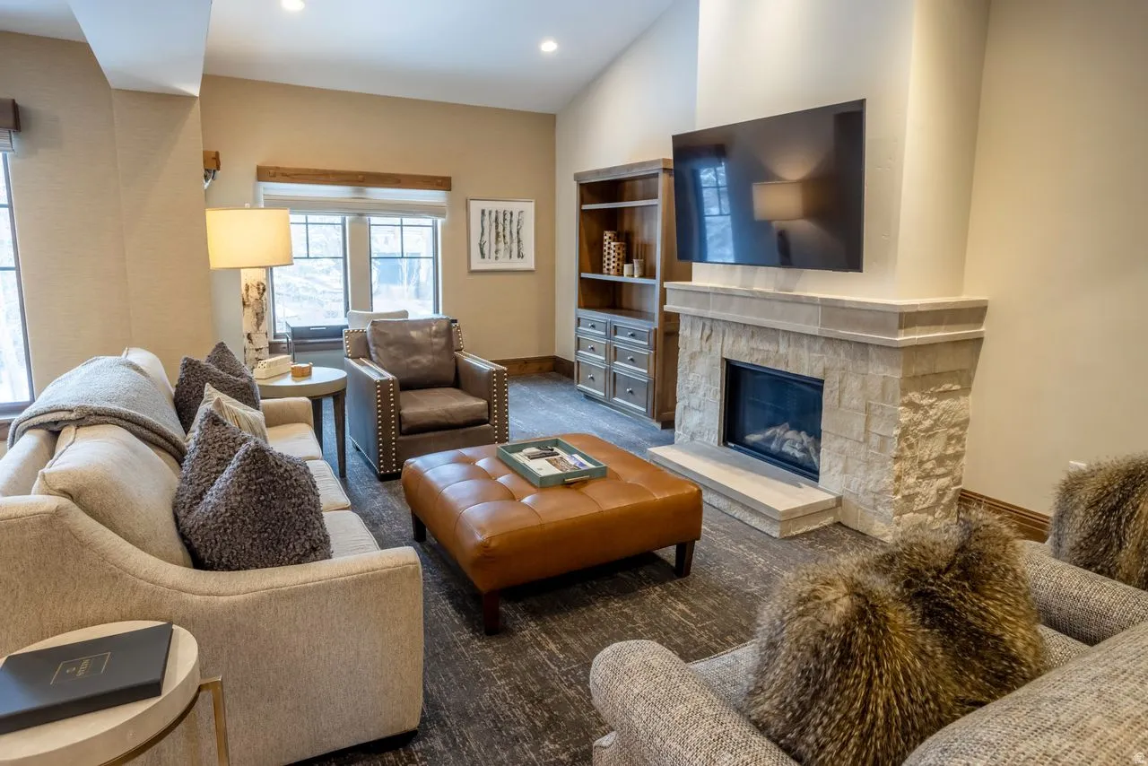Living area featuring a stone fireplace with hearth, built-in shelving, wood-finish flooring, and vaulted ceilings with recessed lighting