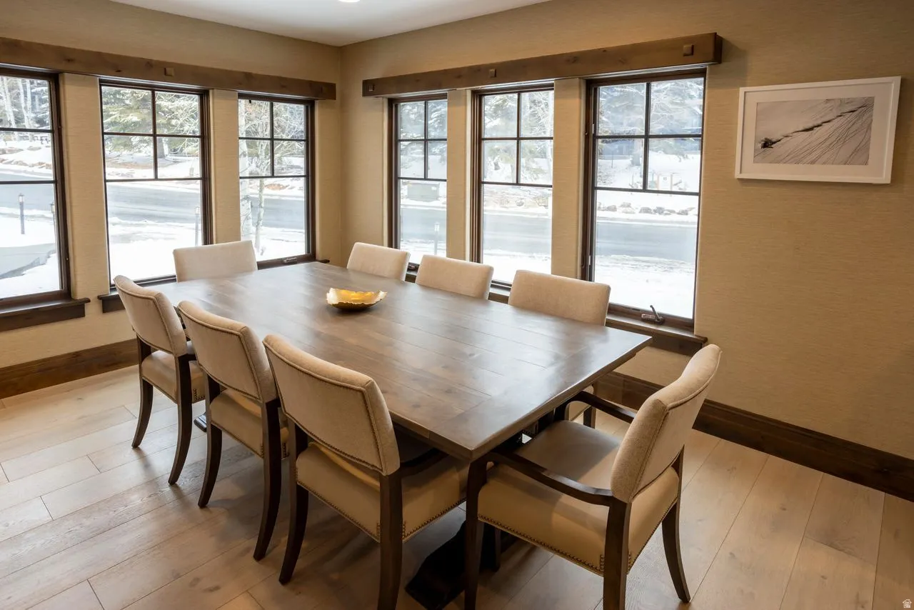 Dining area featuring wood-finish flooring, textured wall covering, and a series of windows with dark trim and grid patterns