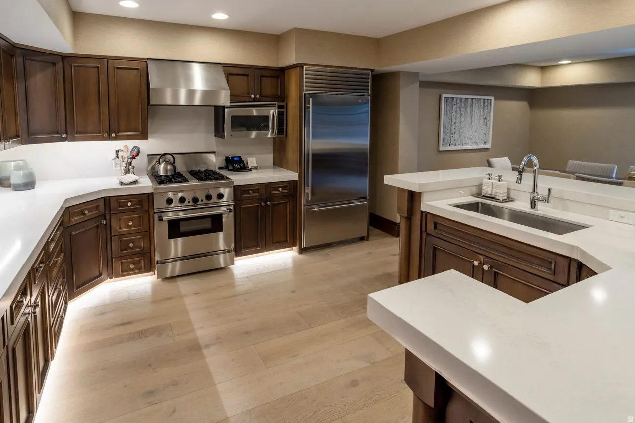 Gourmet kitchen featuring dark wood cabinetry, white countertops, stainless steel appliances including a range with a hood, a large refrigerator, and a built-in microwave