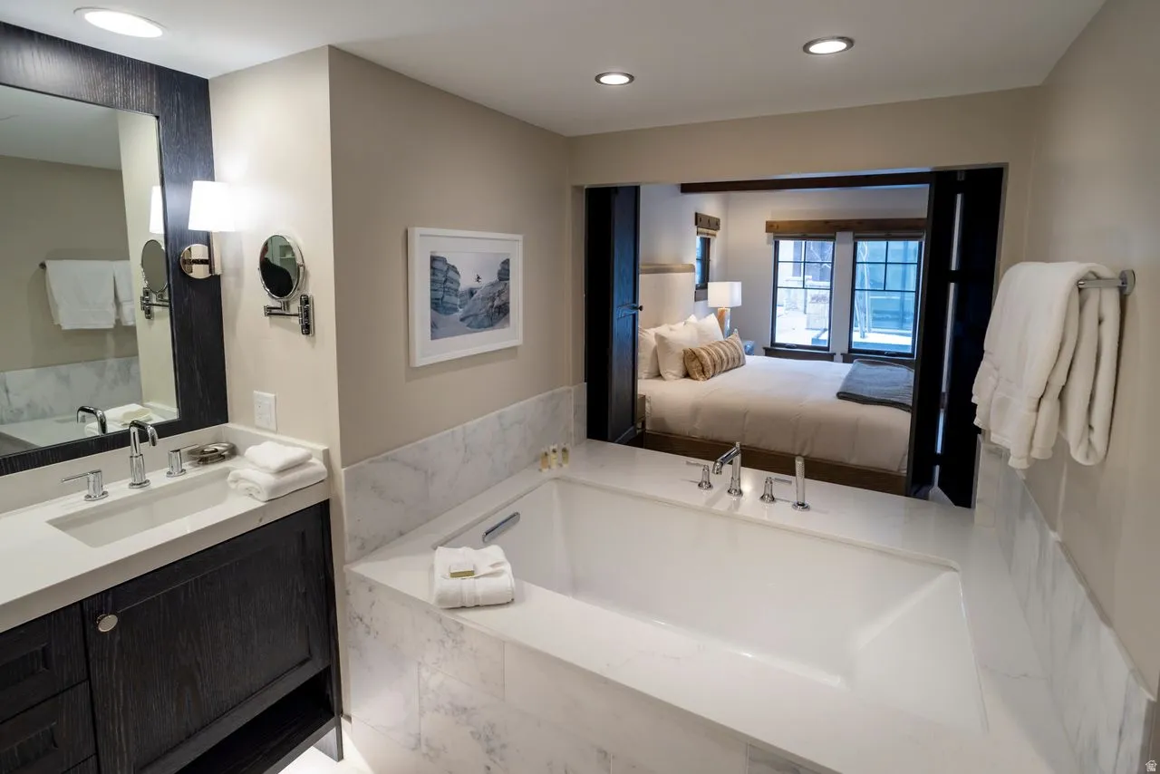 Spacious bathroom featuring a built-in soaking tub, a single vanity with dark wood cabinetry, a large wall mirror, and integrated lighting