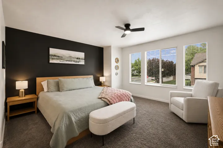 Spacious room featuring a dark accent wall, three large windows with blinds, a ceiling fan, and carpeted flooring