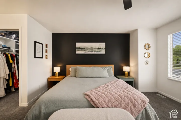Bedroom with a contrasting accent wall, ceiling fan, and carpeted flooring