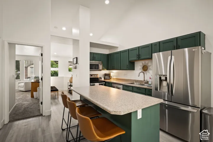 Kitchen featuring green cabinetry, stainless steel appliances, a white subway tile backsplash, and a breakfast bar with a light-colored countertop
