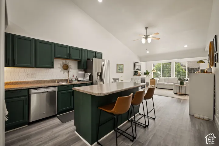 Open-concept kitchen featuring dark green cabinetry, stainless steel appliances, and a central island with bar seating
