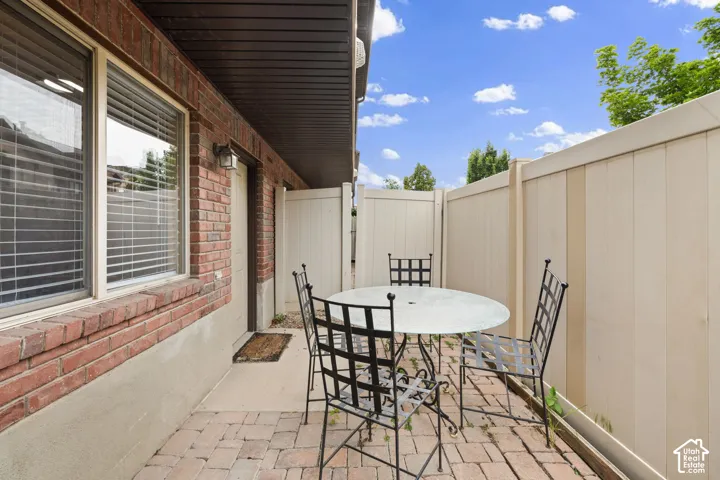 Private brick paver patio area featuring a red brick exterior, a secure privacy fence, and an exterior wall light fixture