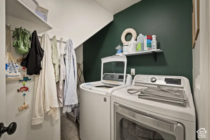 Dedicated laundry space featuring a rich green accent wall, white cabinetry, a built-in shelving unit, and tile flooring