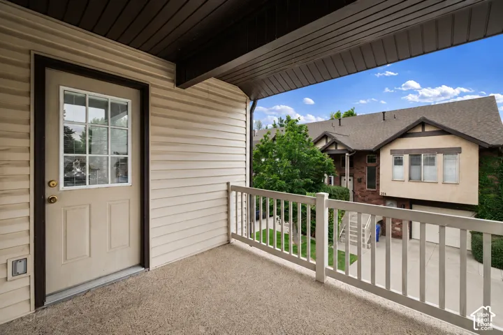 Private outdoor balcony featuring a textured concrete surface, white railing, and exterior wall with horizontal siding