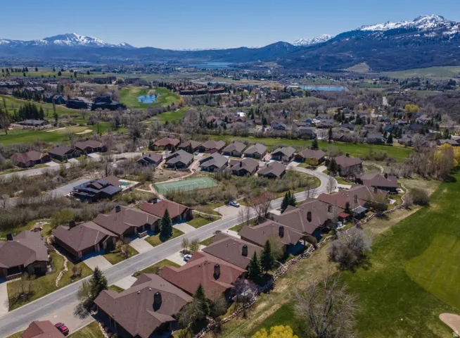 Expansive community featuring numerous single-family residences with brown-tone roofs, a visible tennis court, and a nearby golf course
