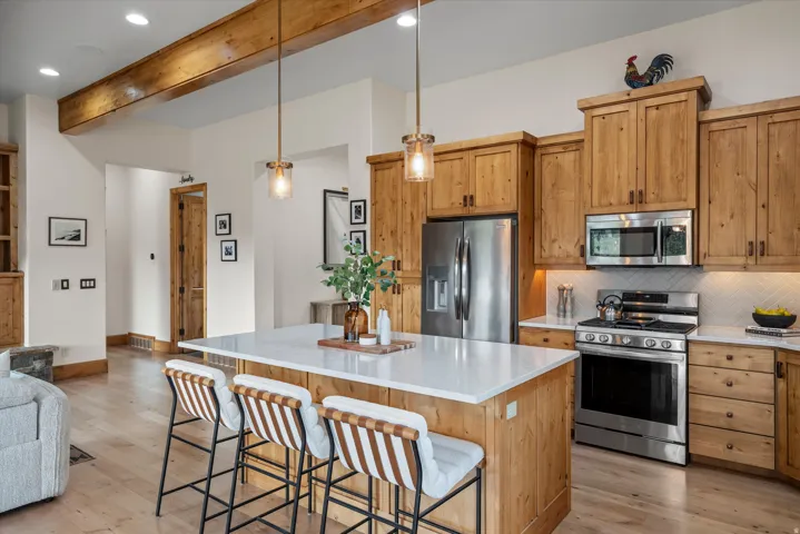 Well-appointed kitchen featuring light wood cabinetry, stainless steel appliances, a white countertop island, pendant lighting, and light wood-finish flooring