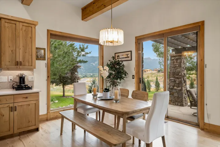 Open-concept dining area featuring wood-finish flooring, exposed wood ceiling beams, and a contemporary chandelier