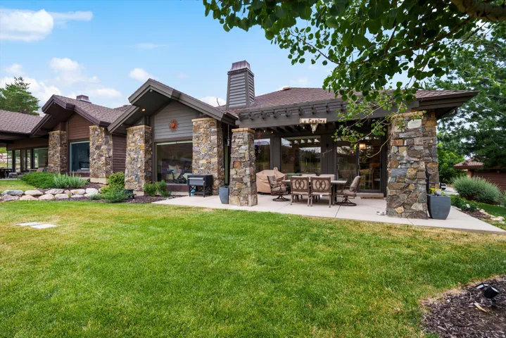 Stone and wood-sided exterior featuring multiple large windows, a covered patio with a pergola, and an expansive lawn