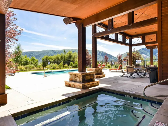 Covered patio area featuring a built-in hot tub, concrete decking, exposed wood beams, and stone accents