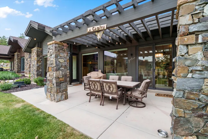 Expansive outdoor living area featuring a concrete patio, a dark wood pergola, and stone pillars