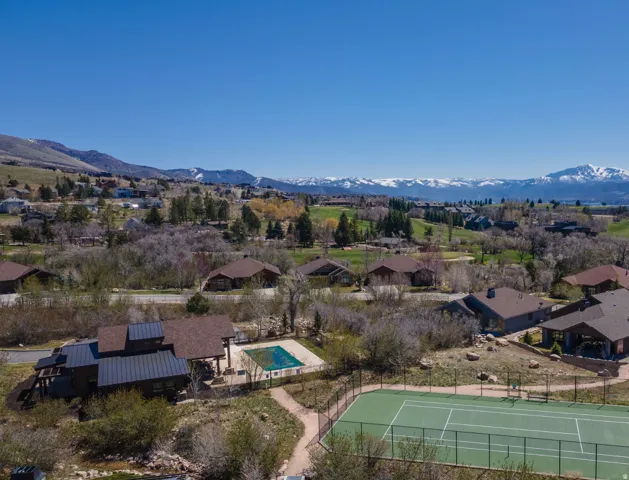 Hardscaped tennis court and fenced swimming pool with surrounding natural landscaping