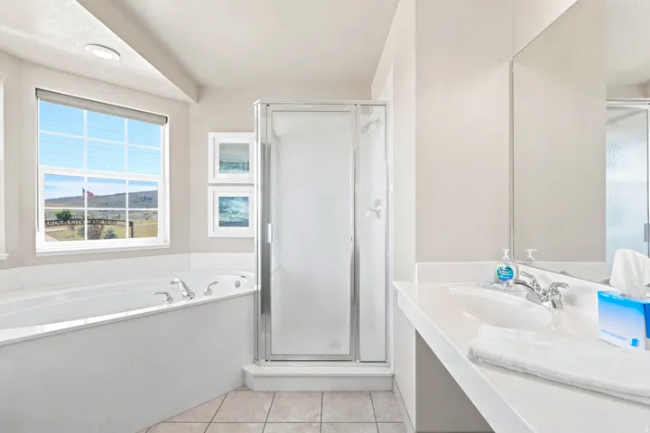 Bathroom featuring a built-in soaking tub, separate shower with frosted glass enclosure, single vanity with integrated sink, and an expansive window with outdoor scenery