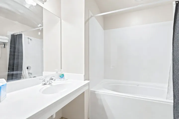 Bathroom featuring a built-in white bathtub, an integrated vanity sink with a laminate countertop, and a large wall-mounted mirror