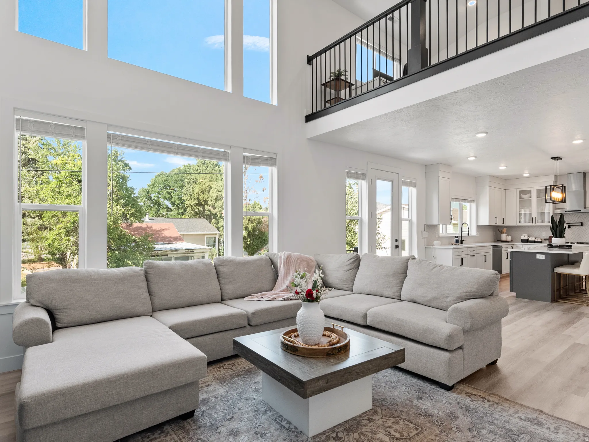 Vaulted ceiling with high windows, open-concept design, wood-finish flooring, recessed lighting, and a kitchen featuring white cabinetry and a central island