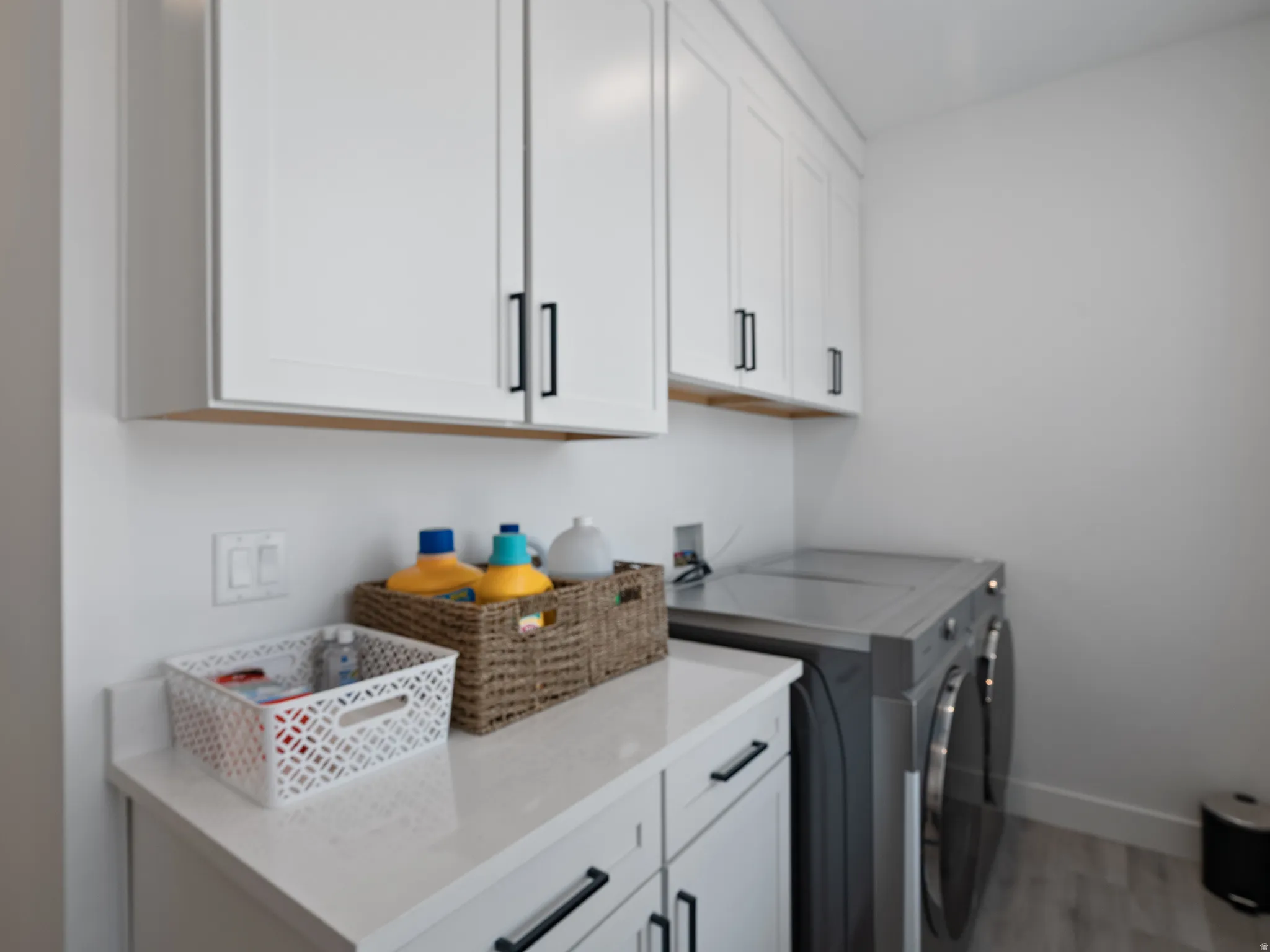 White shaker cabinetry with black hardware, white countertop, and wood-finish flooring