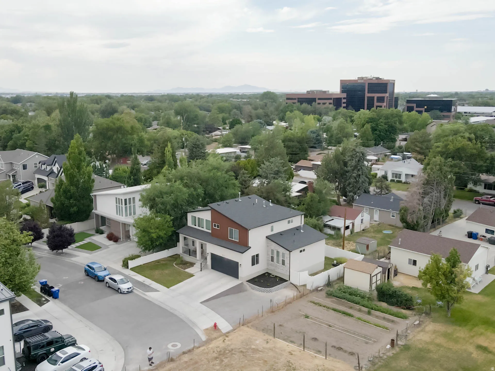 Contemporary multi-level residence featuring a dark gray roofline, mixed material facade with light siding and wood-finish accents, an attached garage, and a concrete driveway