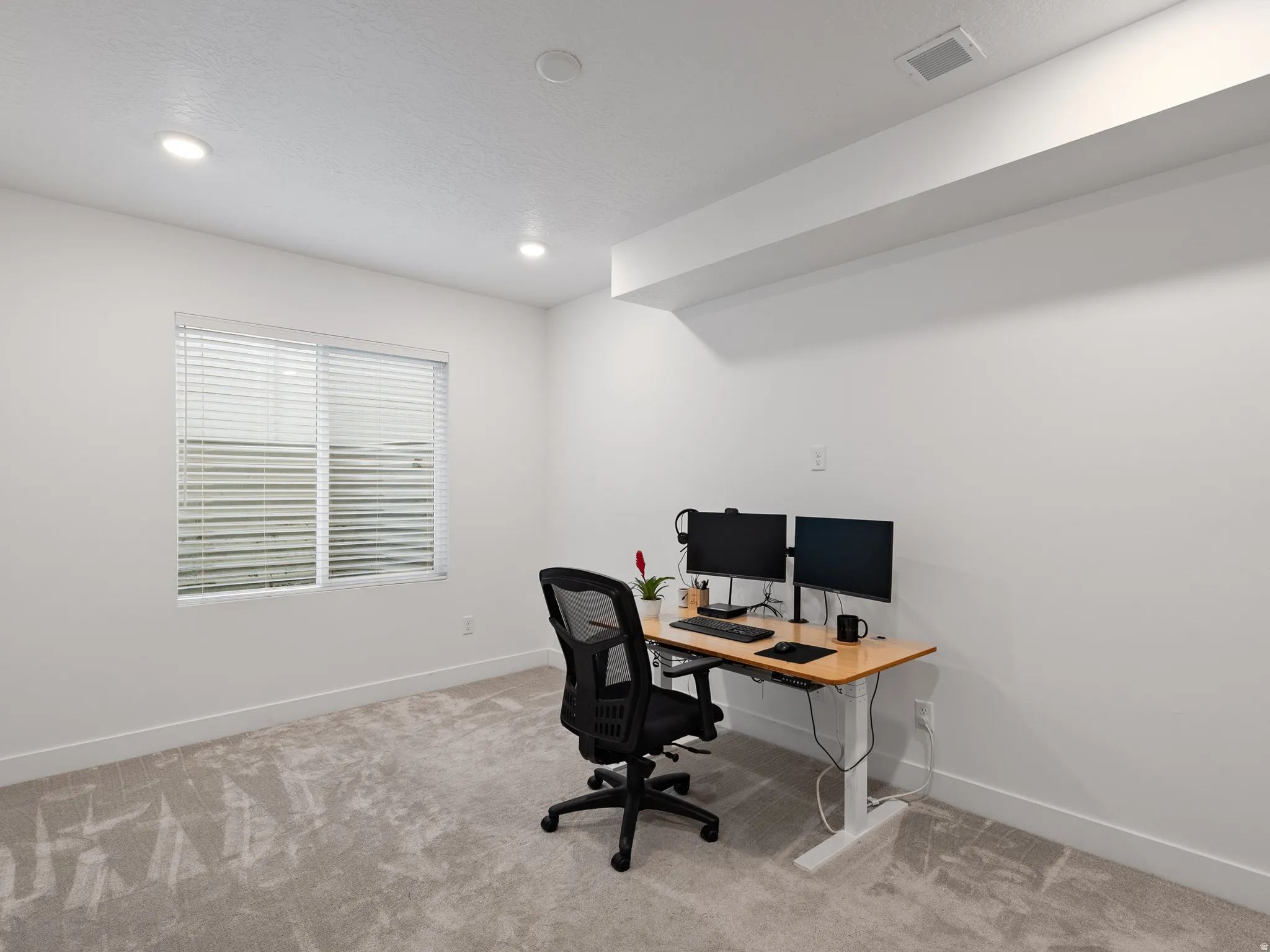 Spacious room featuring a large window with blinds, recessed ceiling lighting, and light-toned carpeting