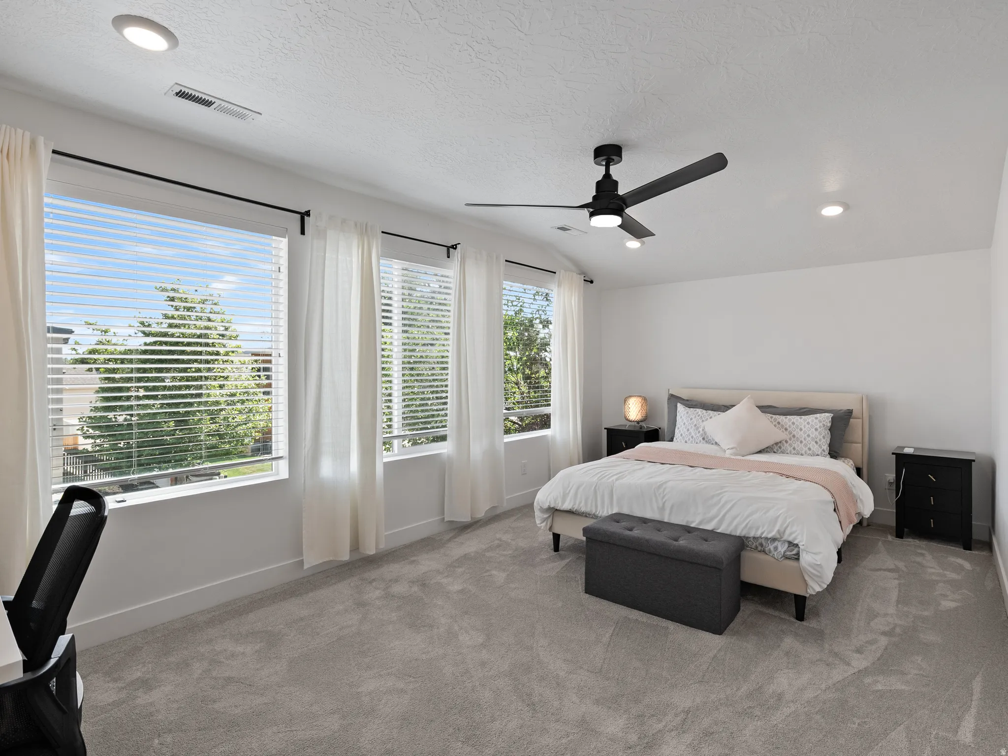 Bright bedroom featuring three large windows with white blinds and curtains