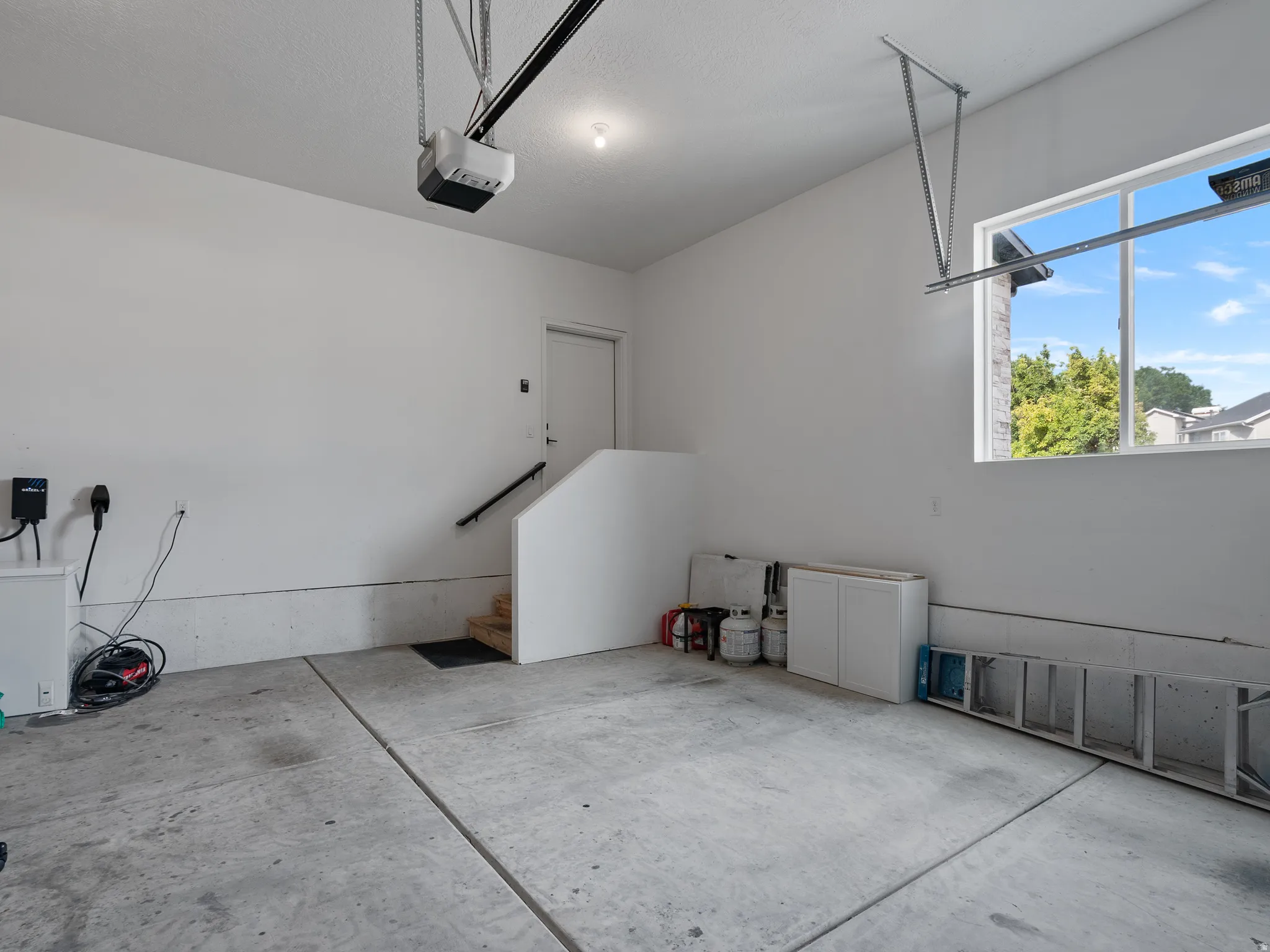 Spacious garage featuring a concrete floor, painted walls, a window for natural light, and an interior door with a handrail