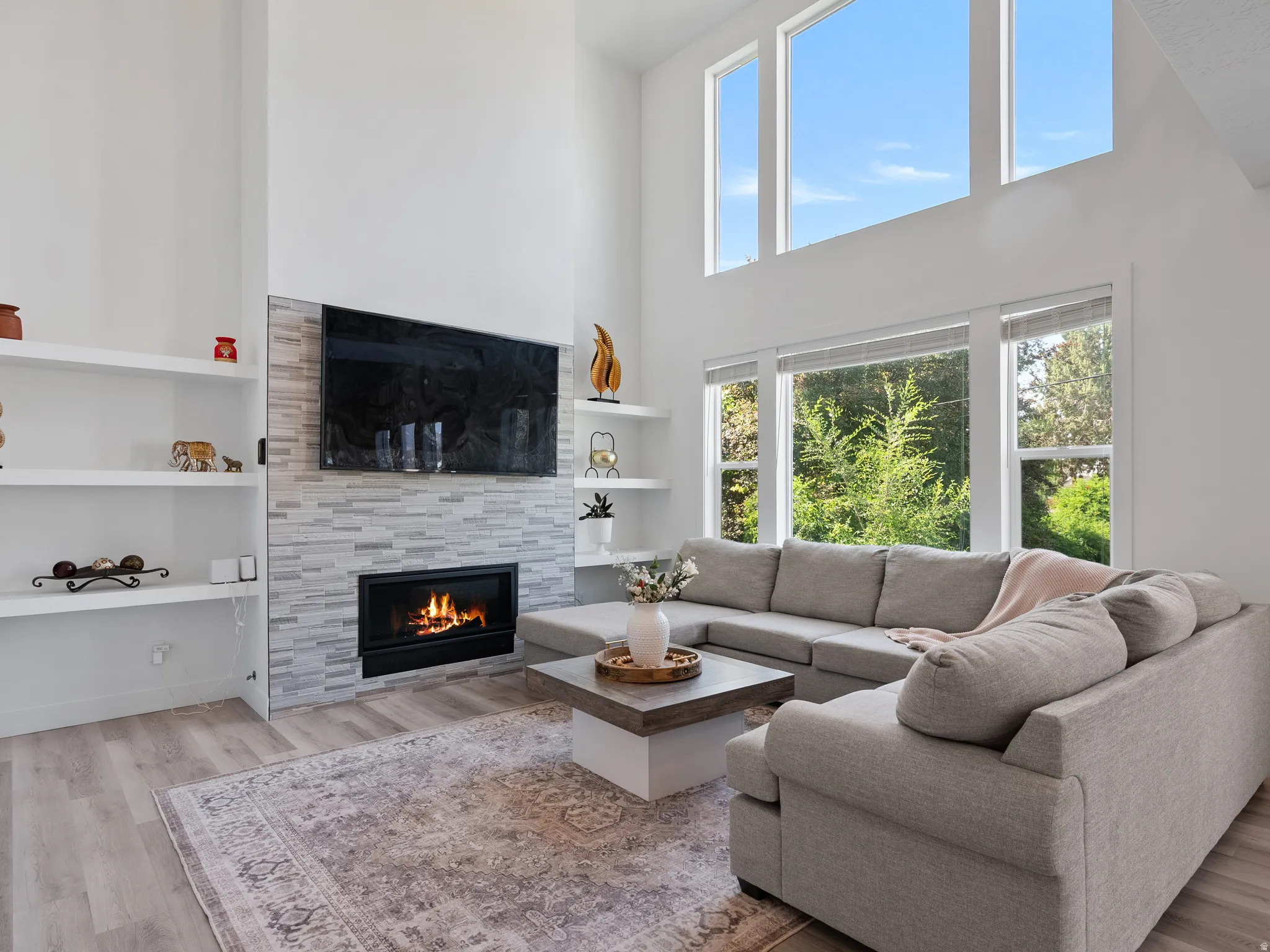 Vaulted ceiling living area featuring a built-in fireplace with a tiled surround, wood-finish flooring, integrated shelving, and large windows
