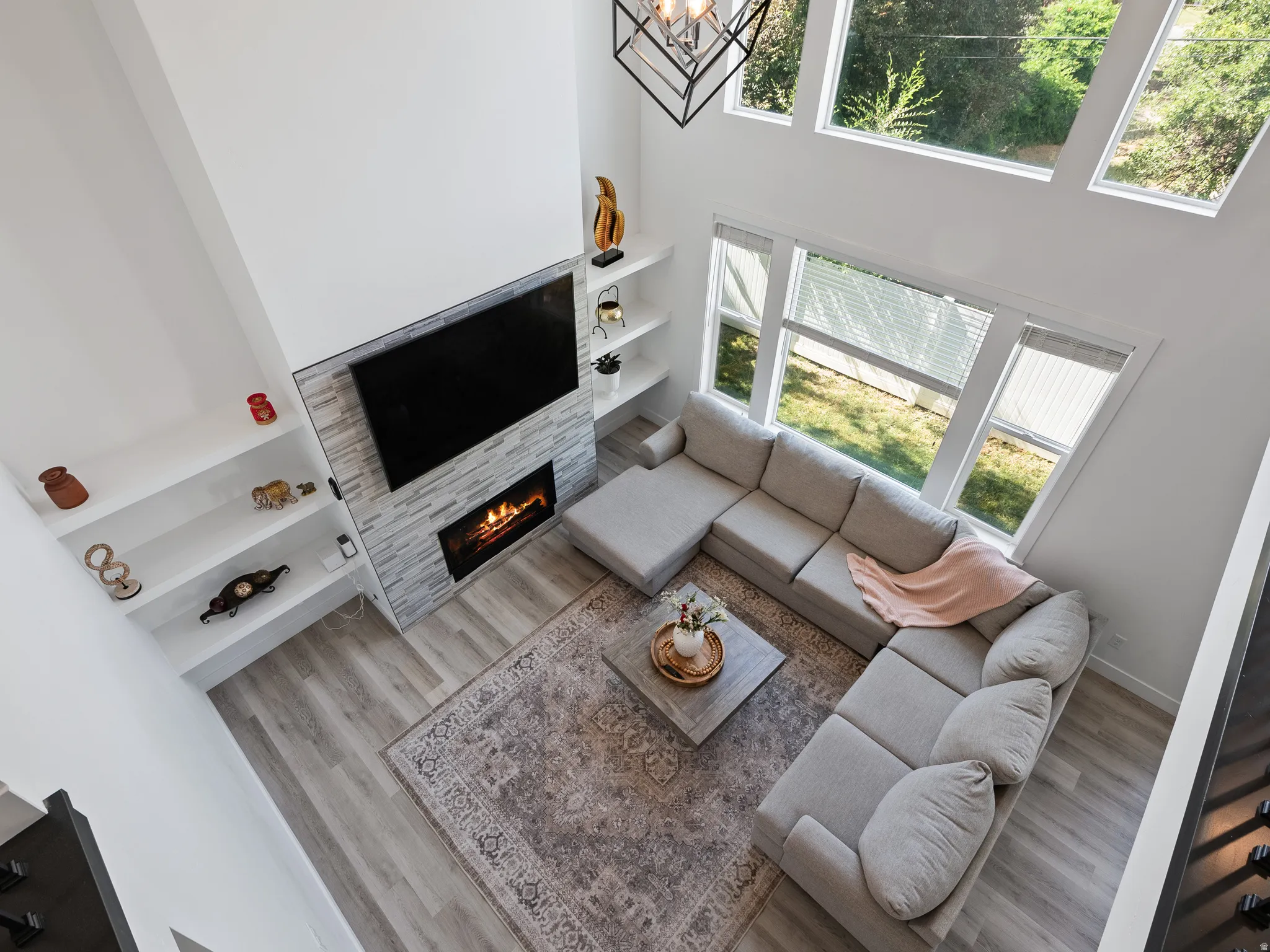 Two-story living area featuring a stone-clad fireplace with an electric insert, built-in shelving, wood-finish flooring, and a multi-pane window configuration