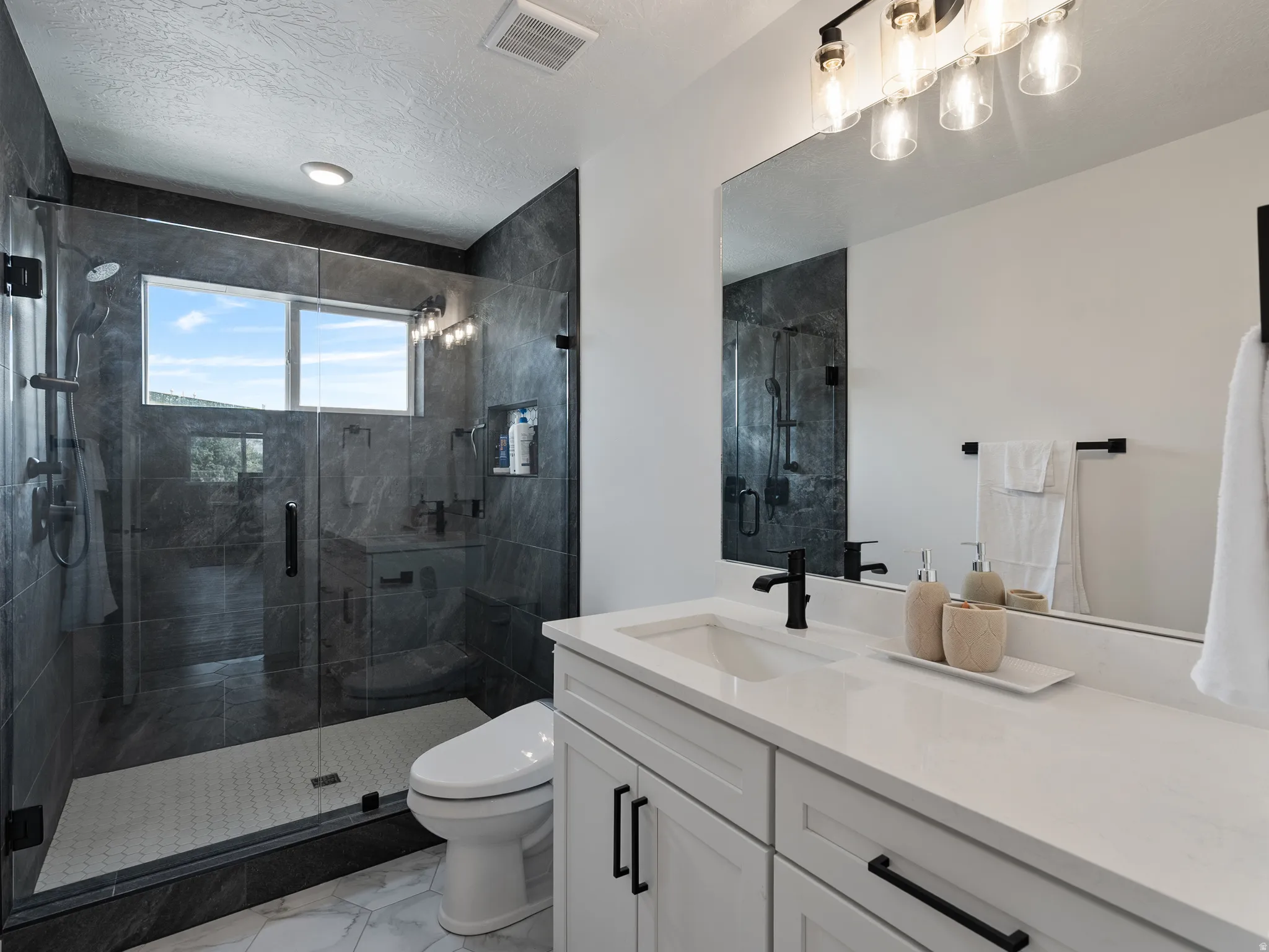 Expansive glass-enclosed shower with dark stone-finish tile surround, a built-in bench, and a window
