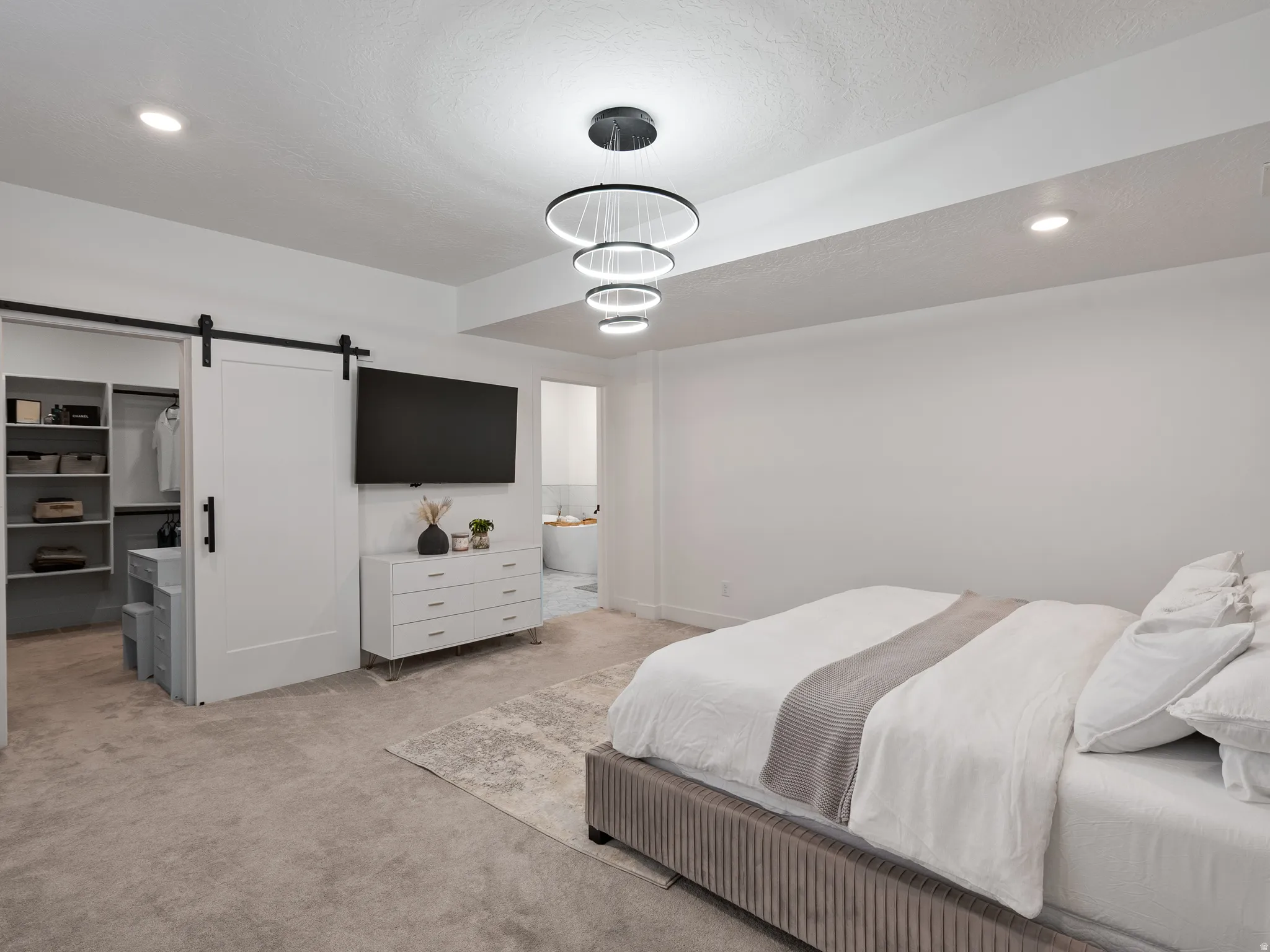Carpeted room featuring a barn door leading to a built-in closet system, recessed lighting, and a contemporary multi-ring chandelier