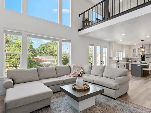 Vaulted ceiling with high windows, open-concept design, wood-finish flooring, recessed lighting, and a kitchen featuring white cabinetry and a central island