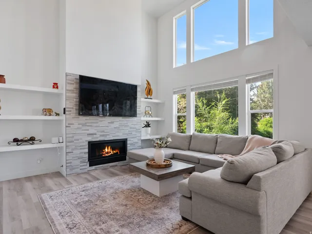 Vaulted ceiling living area featuring a built-in fireplace with a tiled surround, wood-finish flooring, integrated shelving, and large windows
