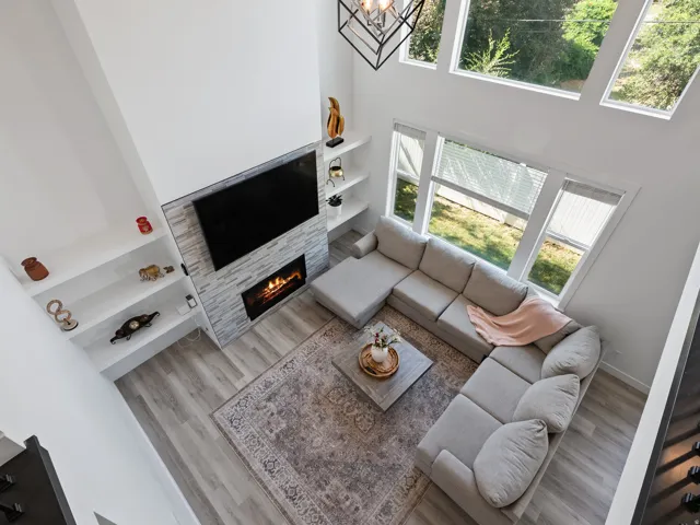 Two-story living area featuring a stone-clad fireplace with an electric insert, built-in shelving, wood-finish flooring, and a multi-pane window configuration