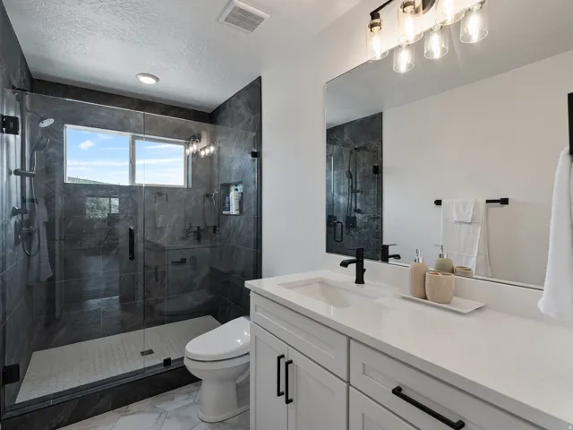Expansive glass-enclosed shower with dark stone-finish tile surround, a built-in bench, and a window