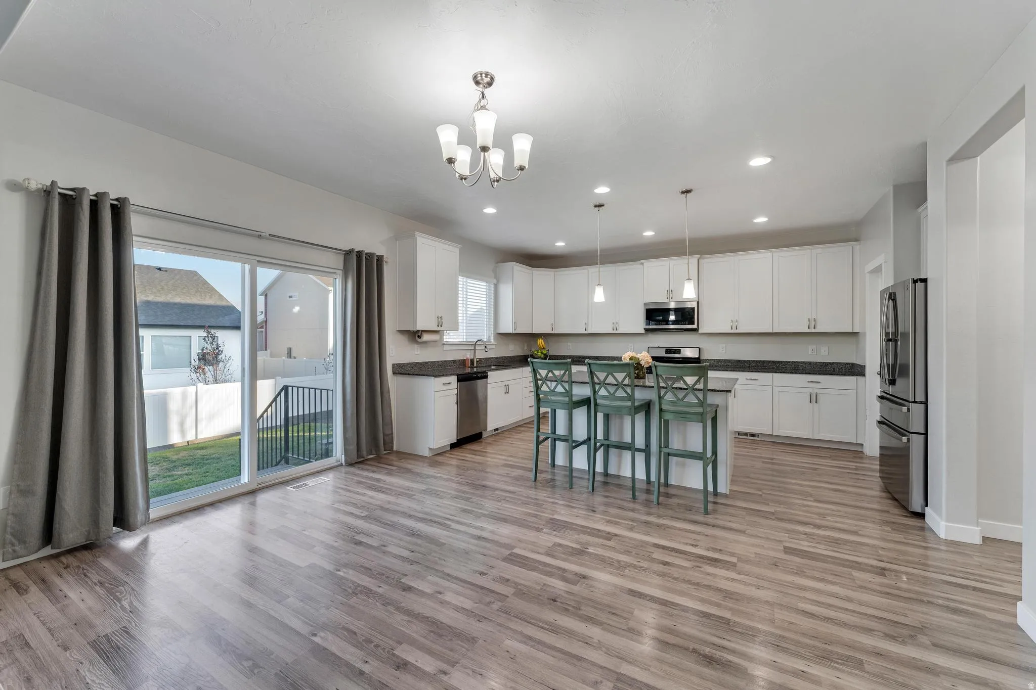 Open concept kitchen featuring white cabinetry, dark countertops, a central island with seating, stainless steel appliances, and wood-finish flooring