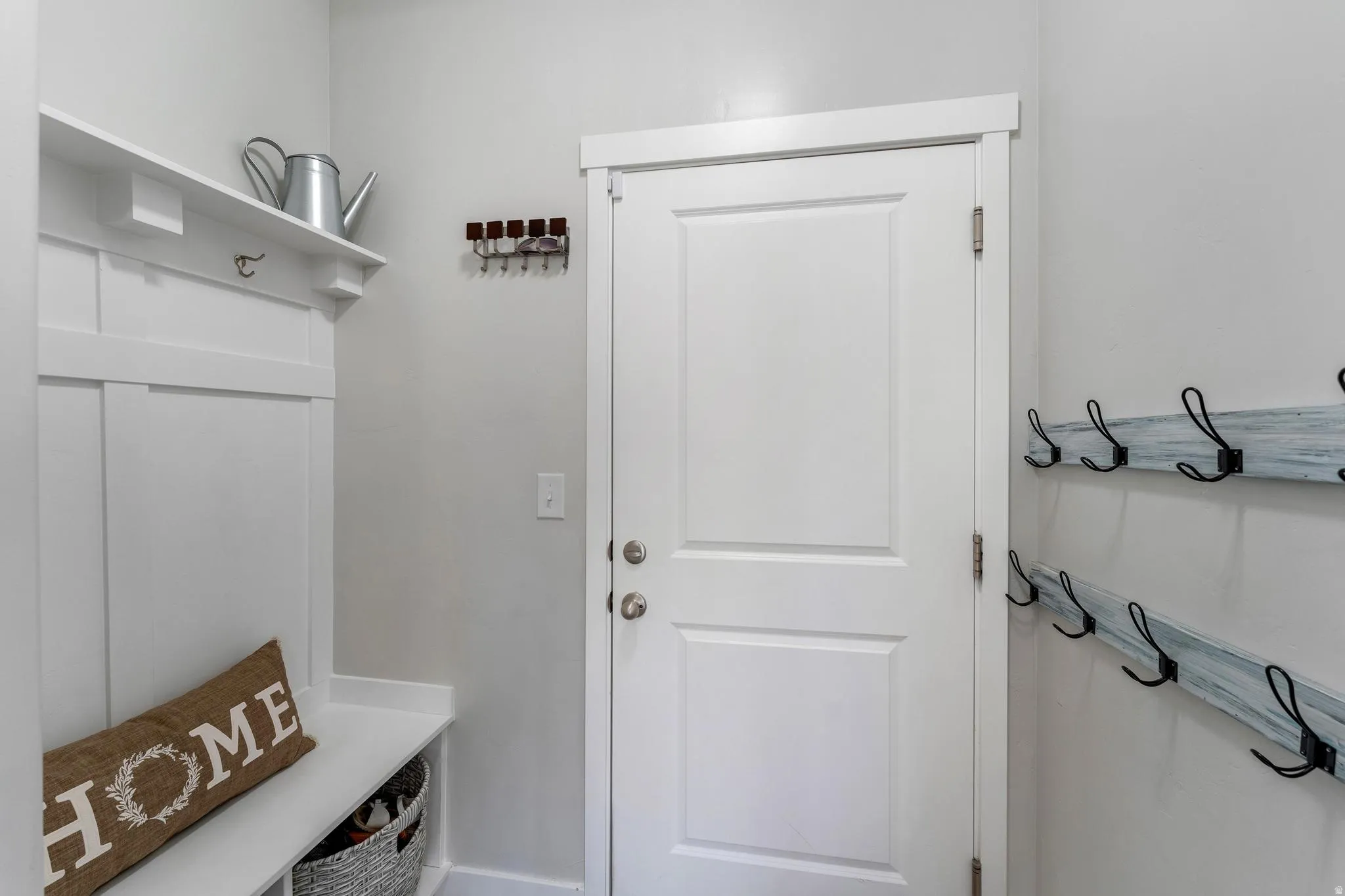 Entryway featuring a white paneled door, built-in coat rack with shelf and bench, and additional wall-mounted coat hooks