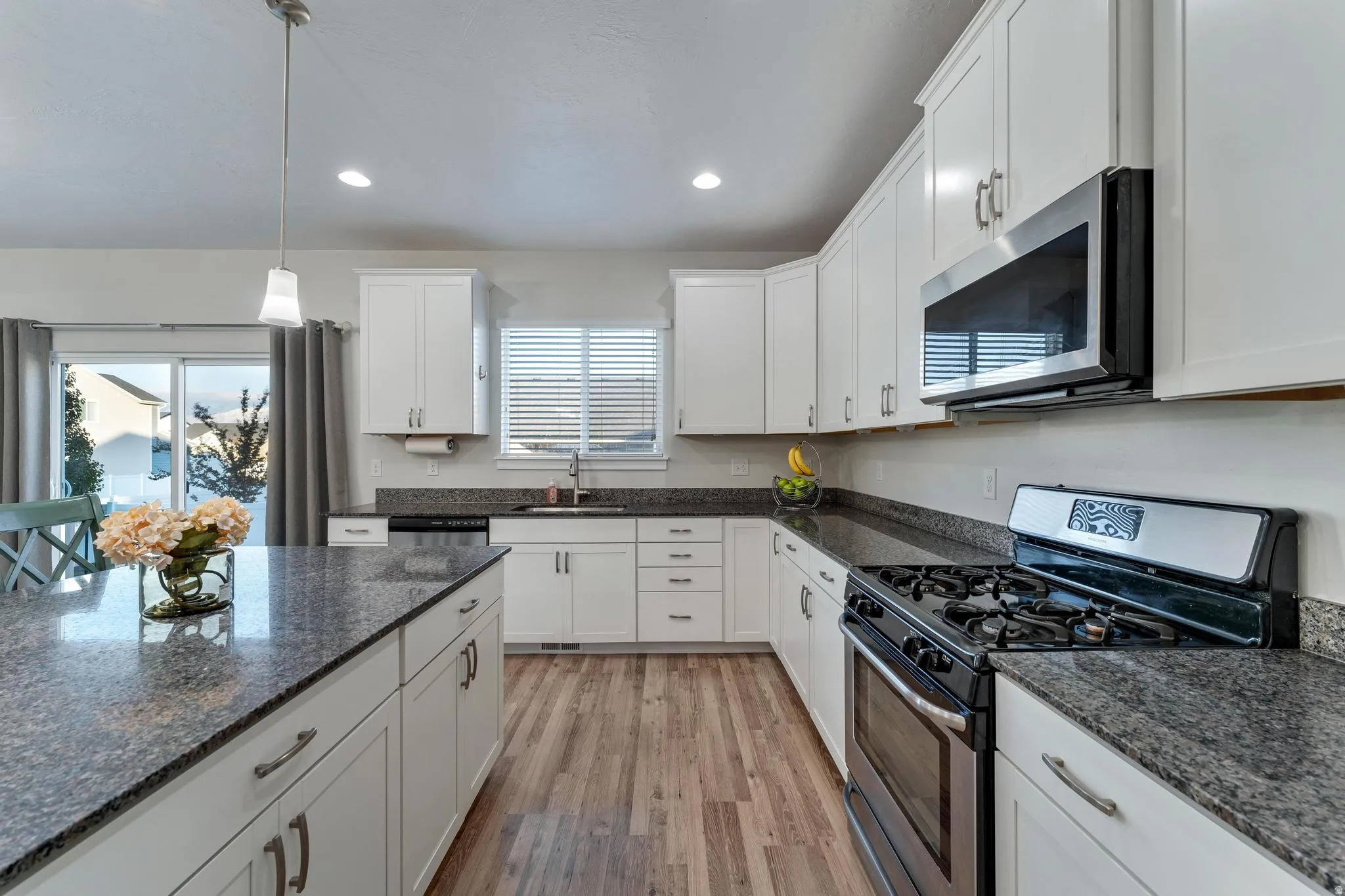 Spacious kitchen featuring white cabinetry, stone-finish countertops, wood-finish flooring, stainless steel appliances, and an island with pendant lighting