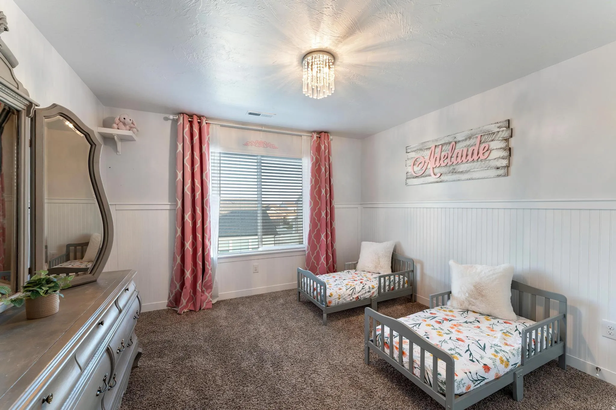 Bright room featuring a window with blinds, a crystal-style flush mount ceiling light, and white wainscoting